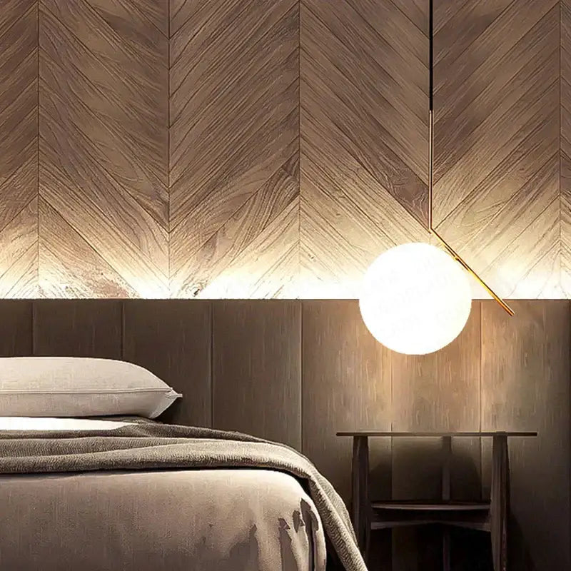 A modern glass ball pendant light with frosted glass globe and gold ring hanging above wooden nightstand for bedroom decor