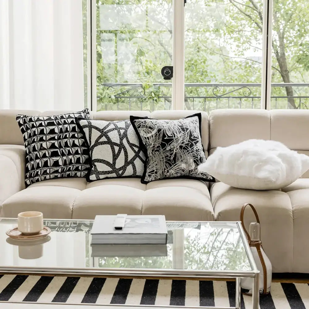 Beige tufted sofa with three black and white geometric embroidered pillow covers and a white cloud shaped pillow