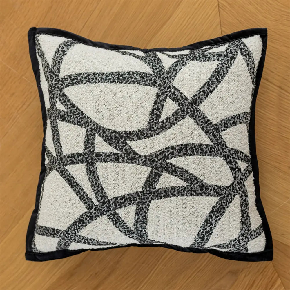 A modern geometric black and white embroidered pillow cover with a textured abstract pattern and solid black border