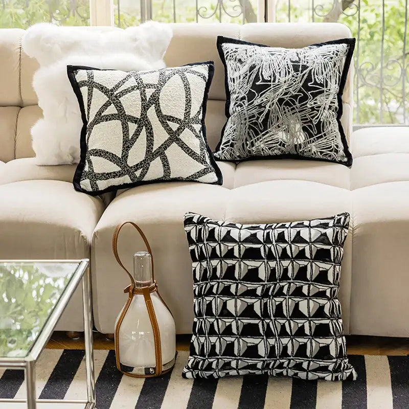 Three black and white geometric embroidered pillow covers on a beige sofa for modern living room decor