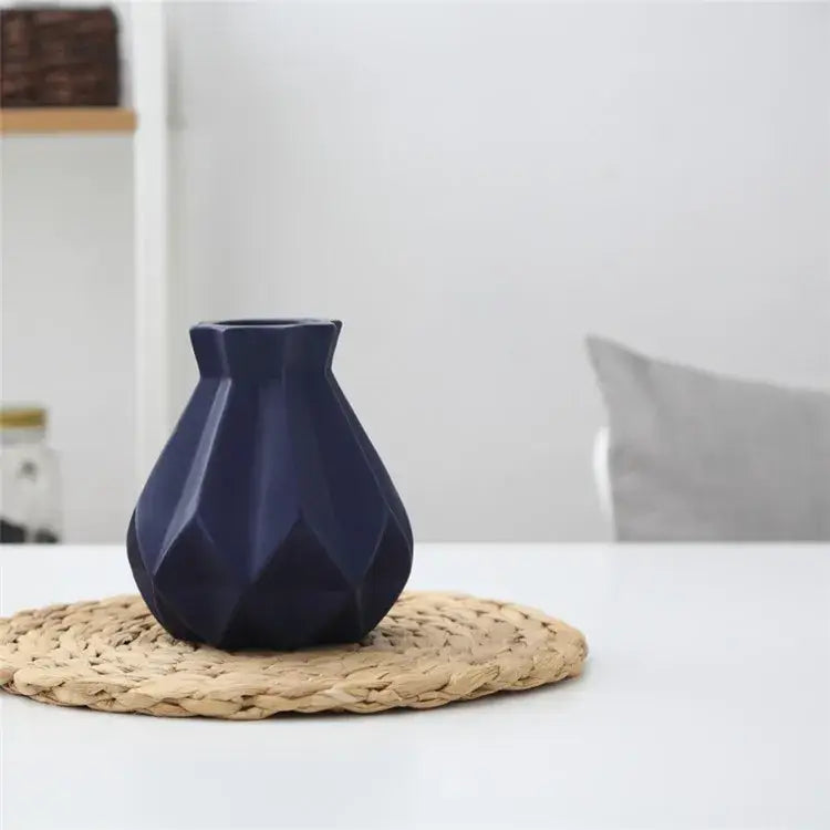 A navy blue decorbites ceramic diamond vase with a geometric faceted design on a woven placemat for living room decor