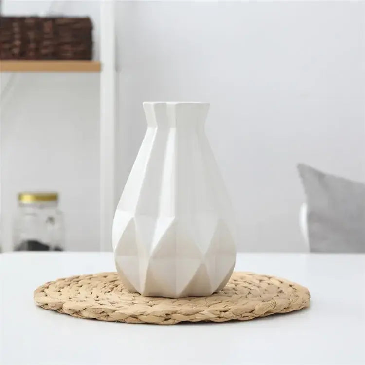 A sleek white decorbites ceramic diamond vase with geometric faceted design on a woven mat for living room decor