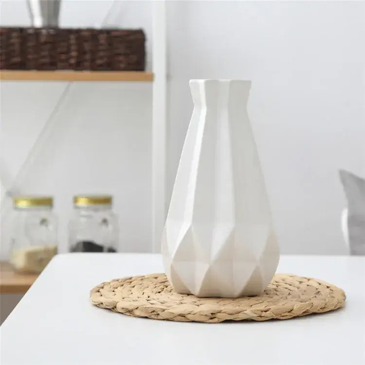 A sleek white decorbites ceramic diamond vase with a geometric faceted design on a woven placemat for living room decor