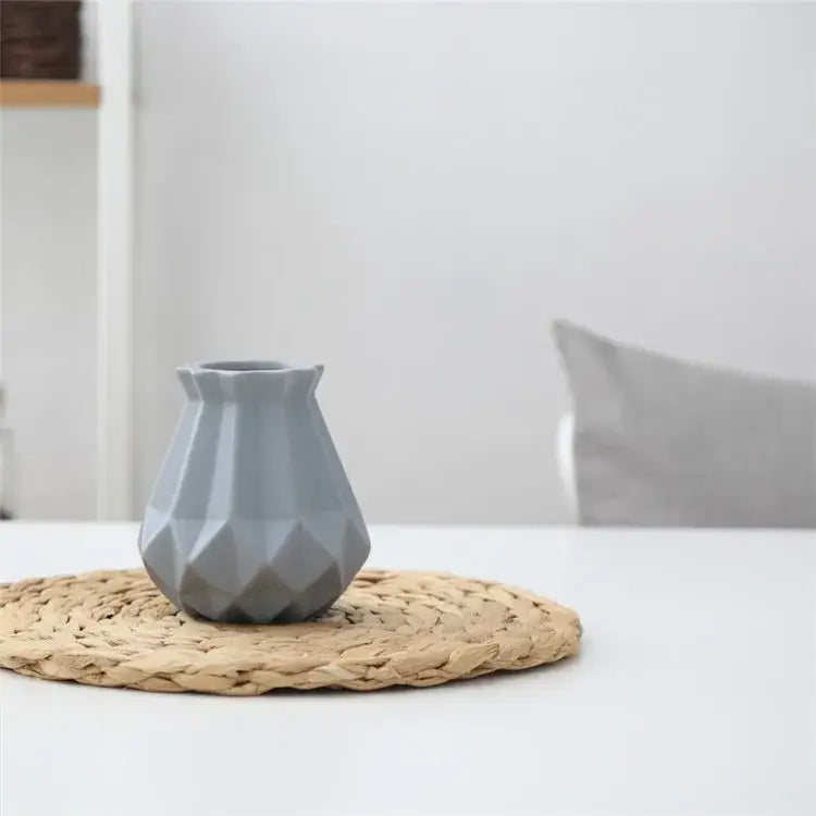 A sleek matte gray decorbites ceramic diamond vase with geometric facets on a woven placemat for living room decor