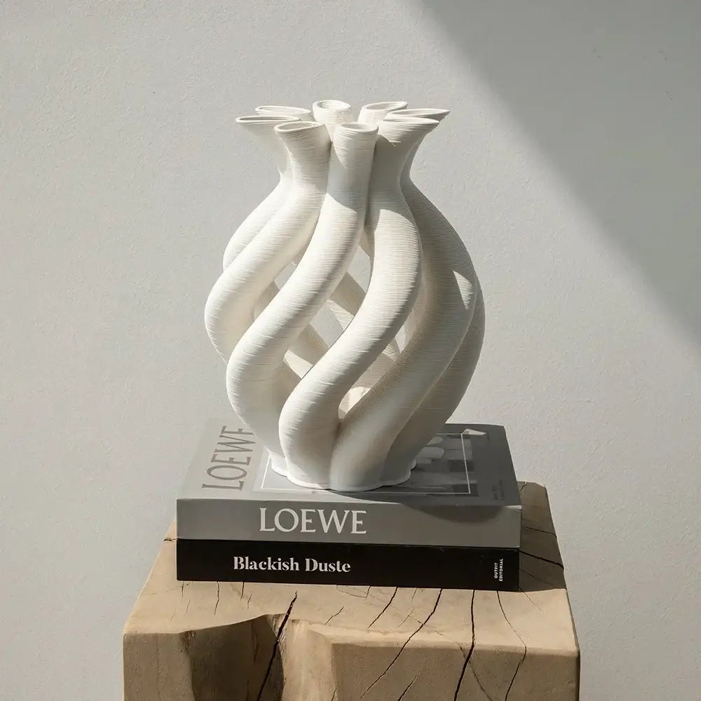 A sleek white geometric ceramic spiral vase with twisted design on stacked Loewe books for modern living room decor
