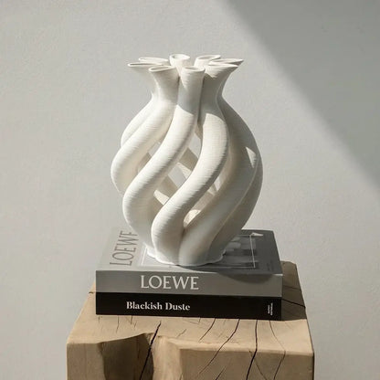 A sleek white geometric ceramic spiral vase with twisted design on stacked Loewe books for modern living room decor