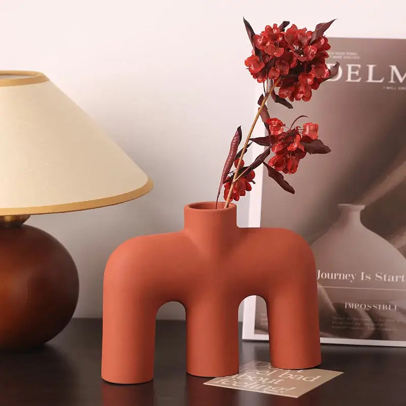 Terracotta-colored modern geometric ceramic vase with three curved legs and open top for living room decorbites geometric decor