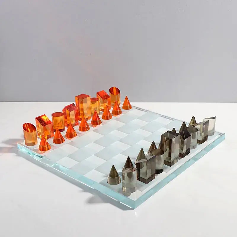 Transparent glass chess set with vibrant orange and metallic silver pieces on a geometric crystal decorbites board