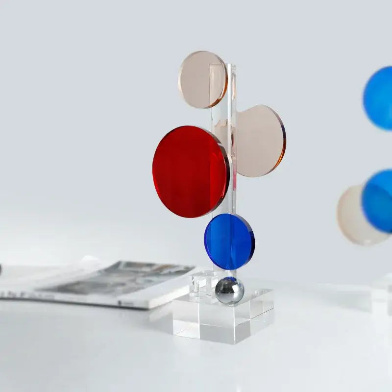 A modern geometric crystal circle sculpture with translucent red blue and beige discs on clear acrylic for home decor