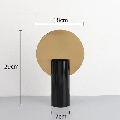 Black geometric cylinder vase with matte finish and circular gold base holding pink artificial flowers decorbites decor