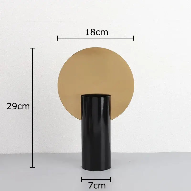 Black geometric cylinder vase with matte finish and circular gold base holding pink artificial flowers decorbites decor
