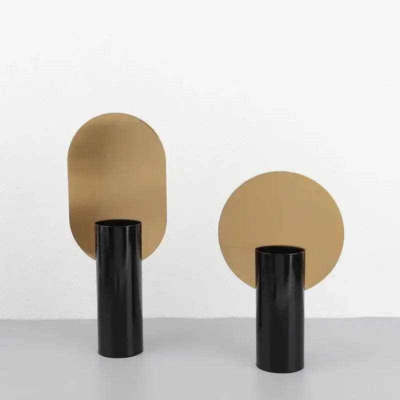 Two minimalist black geometric cylinder vases with polished gold backplates featuring pink artificial flowers decorbites decor
