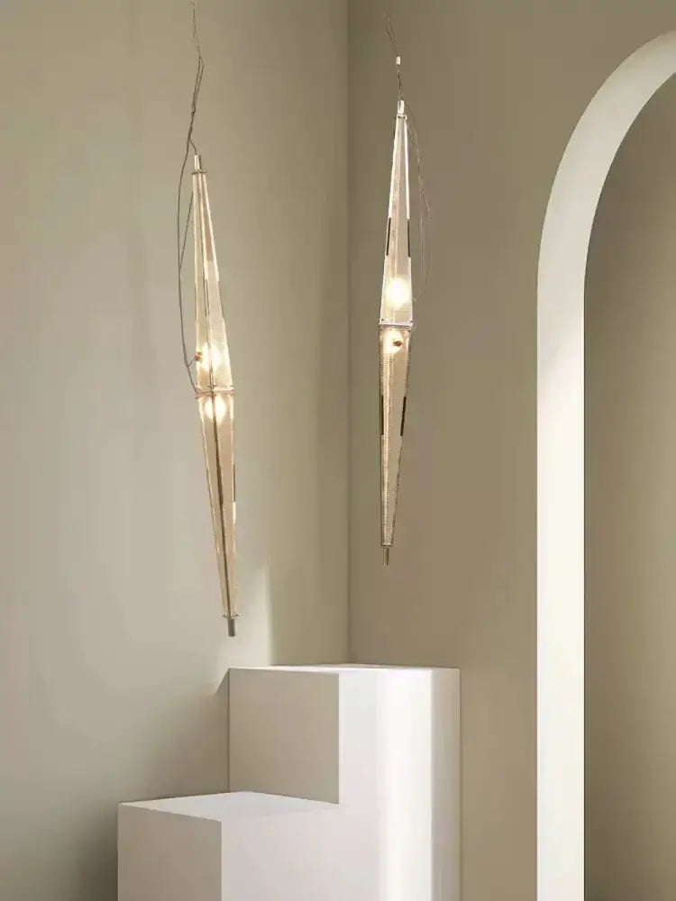 Two slender glass cone chandelier pendant lamps with translucent glass and metallic accents hang in a dining room