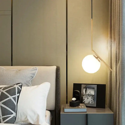 A modern minimalist glass pendant light with frosted spherical bulb and gold arms for bedroom bedside chandeliers
