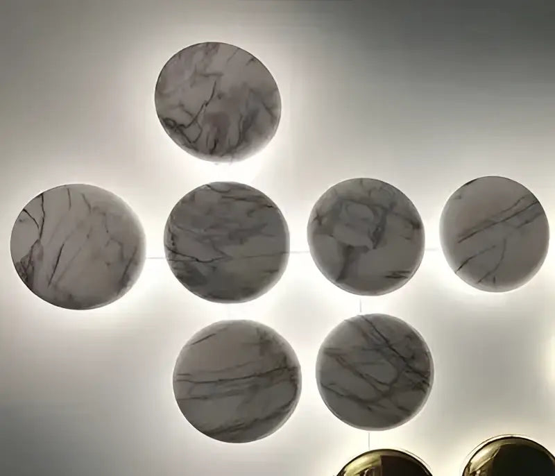 Circular marble wall art with gray and white veining arranged geometrically paired with glossy gold led wall sconces