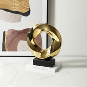 Shiny gold abstract geometric gold ring hollow sculpture with intertwined loops on black base for living room decor
