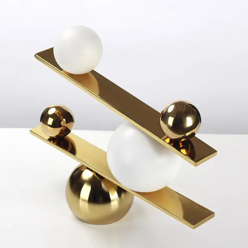 Modern geometric golden ball seesaw ramp living room sculpture with intersecting gold bars and polished white spheres decorbites geometric golden