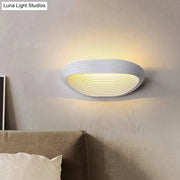 Modern geometric white wall light with concentric ridges providing warm white light for bedroom use