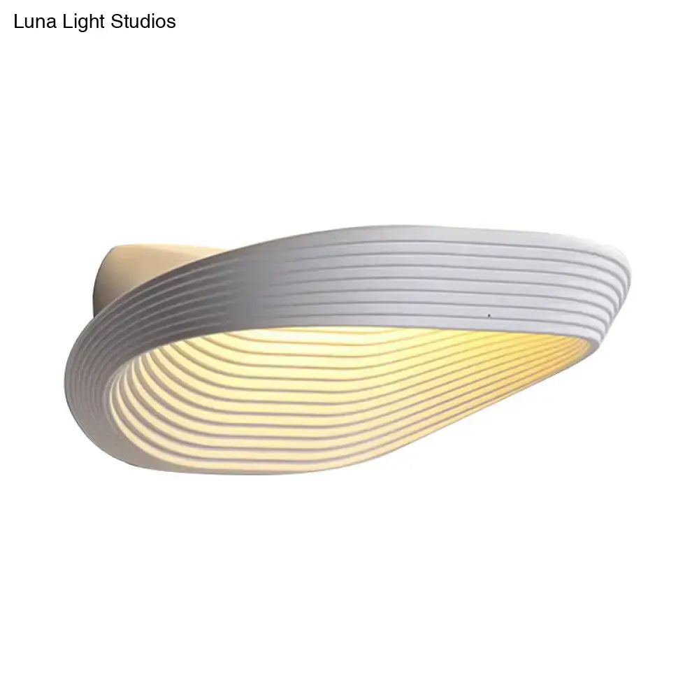 Modern white wall light with sleek curved design and concentric ridges emitting warm white light for bedroom use