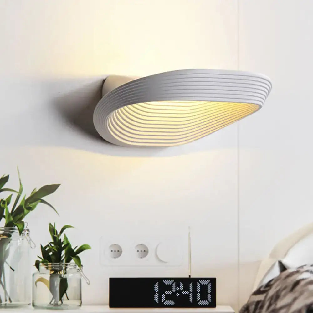 Modern white wall light with sleek curved design and concentric ridges producing warm white light for bedrooms
