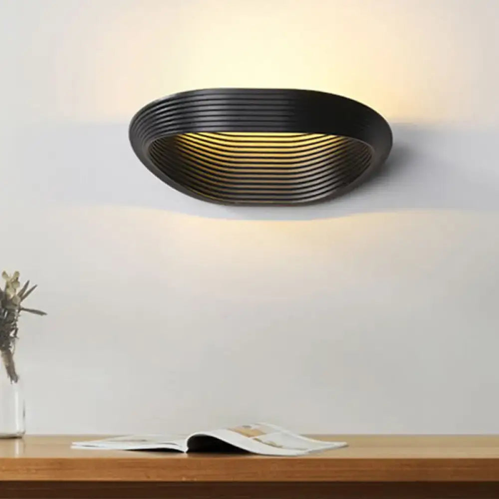 Black oval wall light with concentric ridged design emitting warm white light for modern bedroom decor