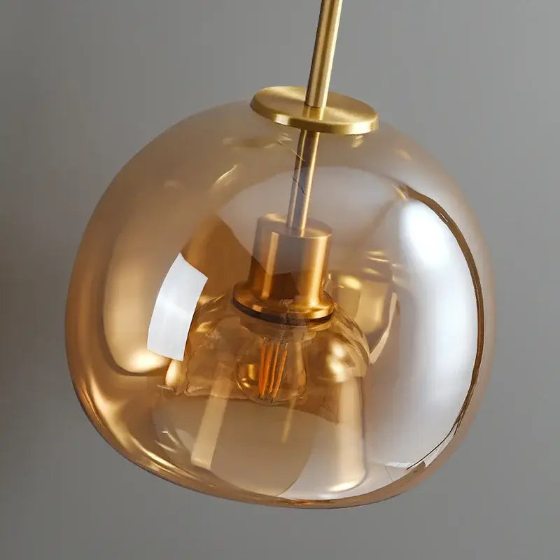 A sleek amber glass ball led ceiling light with polished brass finish and exposed filament bulb for bedroom decorbites lighting