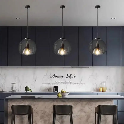 Three modern decorbites glass ball LED pendant lights with clear glass globes and exposed filament bulbs hang above kitchen island