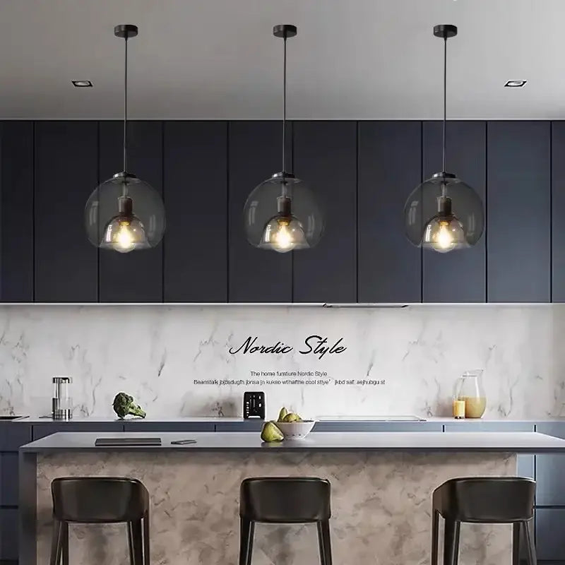 Three modern decorbites glass ball LED pendant lights with clear glass globes and exposed filament bulbs hang above kitchen island