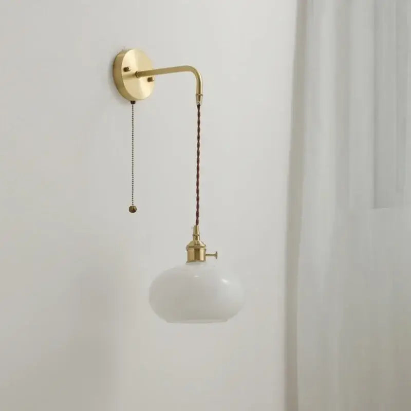 A sleek modern glass copper led wall light with curved brass arm and white opal glass shade for bedroom use