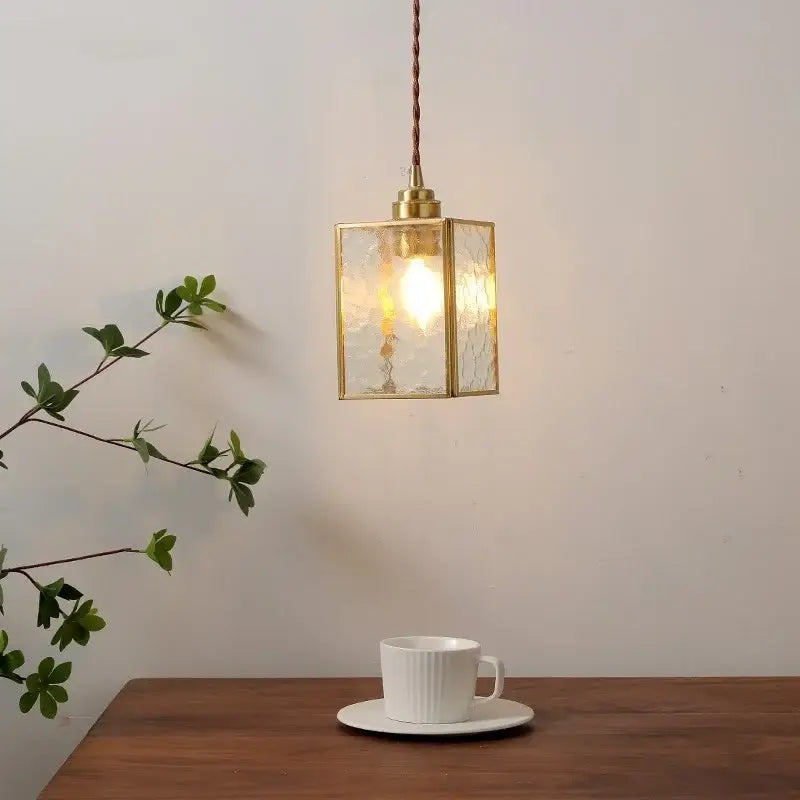A warm-toned glass copper pendant light with textured panels hangs above a wooden table for kitchen island use