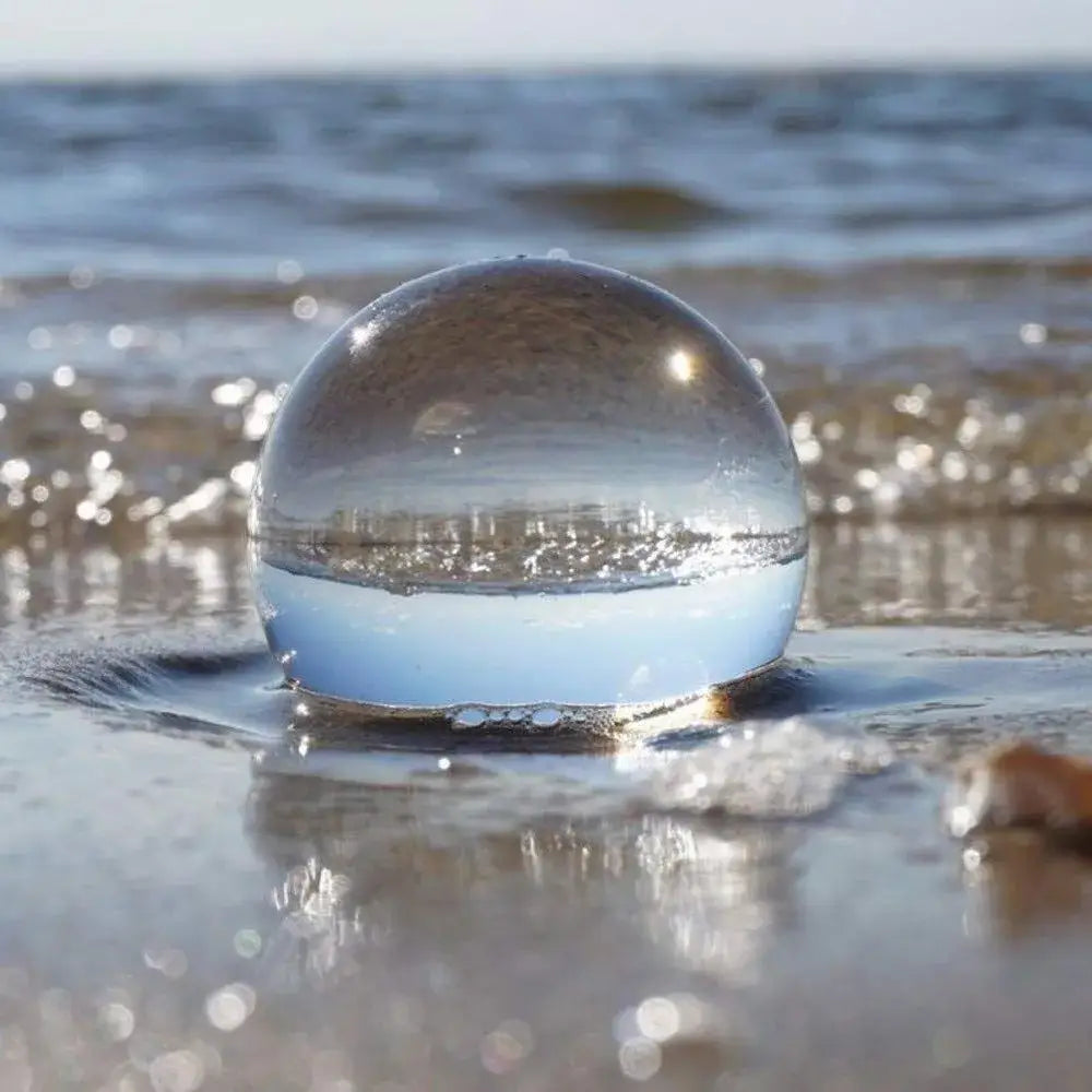 A clear glass crystal ball resting on wet sand used as a modern photography prop and living room decor