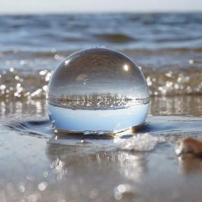A clear glass crystal ball resting on wet sand used as a modern photography prop and living room decor