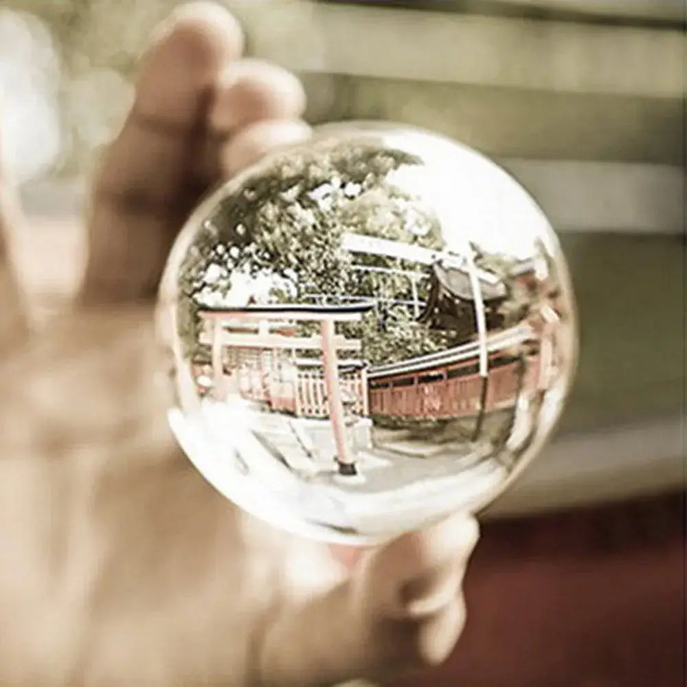 A clear spherical glass crystal ball held in hand reflecting a traditional japanese torii gate and trees for modern decor