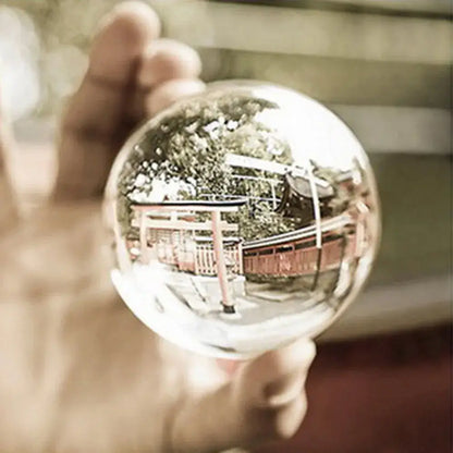 A clear spherical glass crystal ball held in hand reflecting a traditional japanese torii gate and trees for modern decor