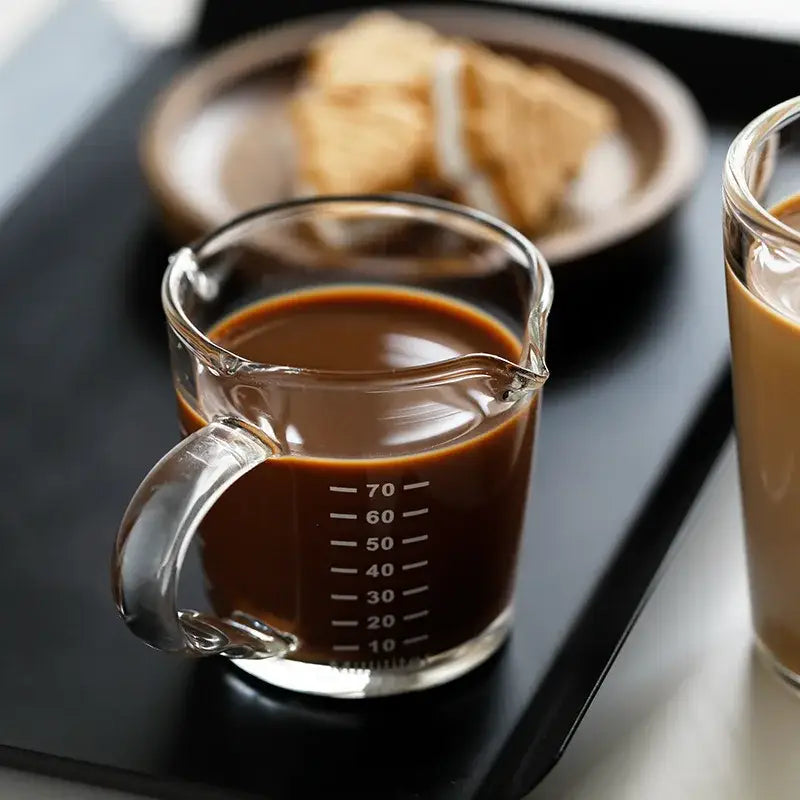 Modern glass cup measuring jug with wooden handle filled with dark brown liquid for milk latte jug use