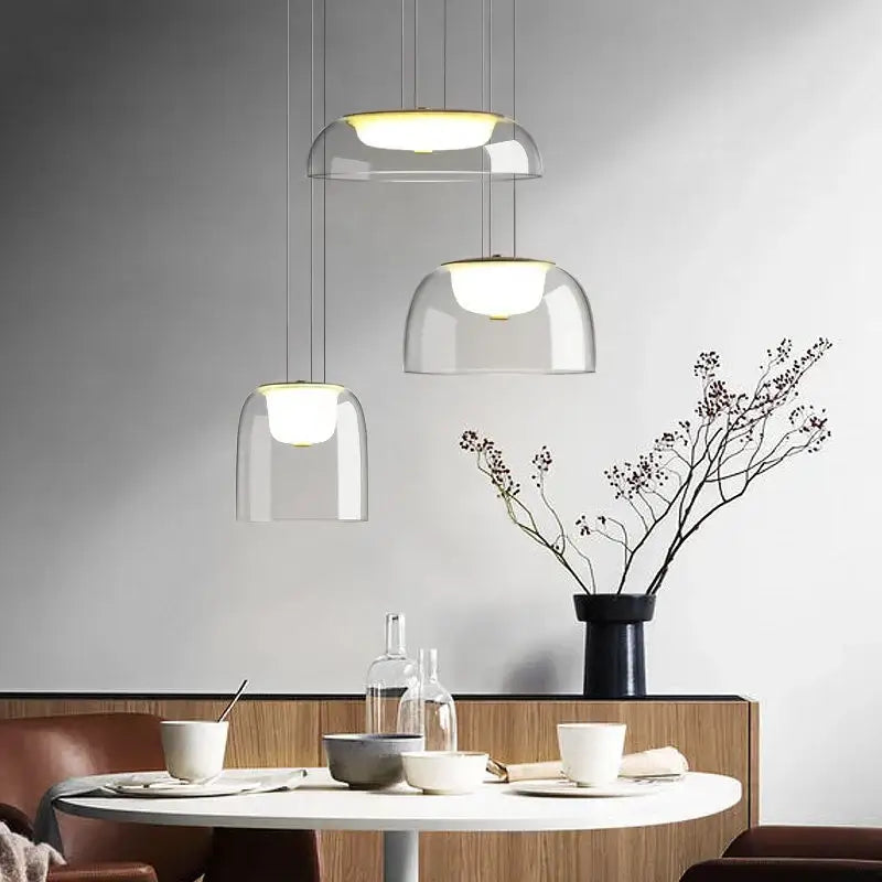 Three modern glass pendant lights with clear glass domes and wood fixtures hang above a dining table
