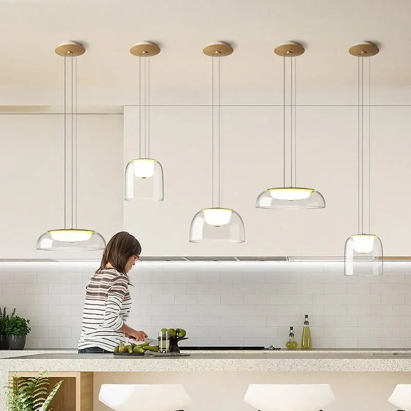Five modern glass pendant lights with clear glass domes and warm wood fixtures for dining room lighting