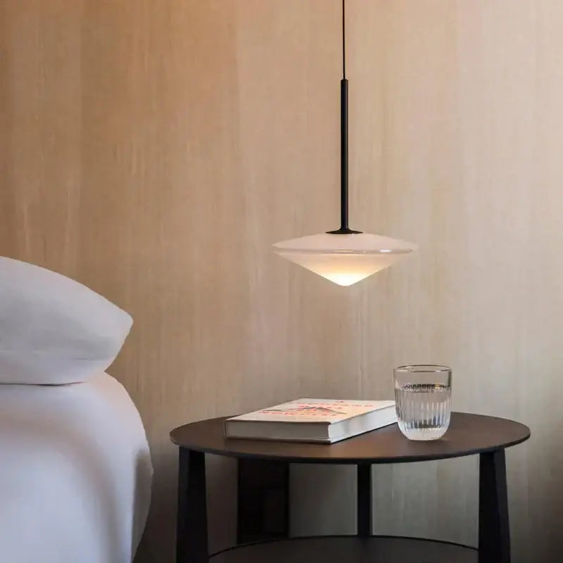 Modern black flying saucer chandelier with frosted glass shade hanging above dark wood side table