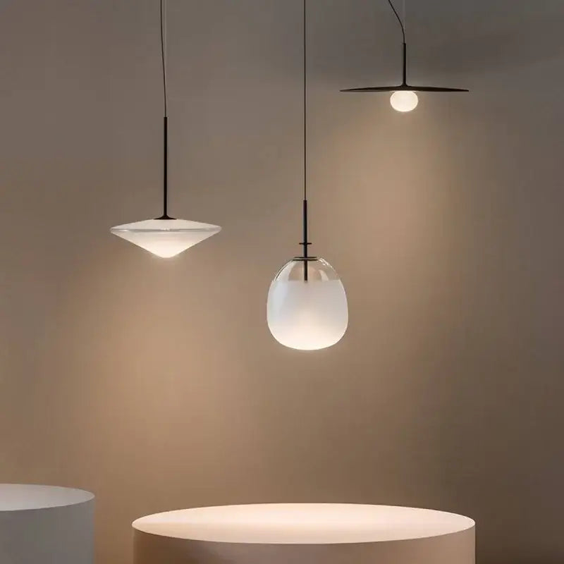 Three minimalist glass flying saucer chandelier pendant lights with frosted glass shades and black metal fixtures hanging