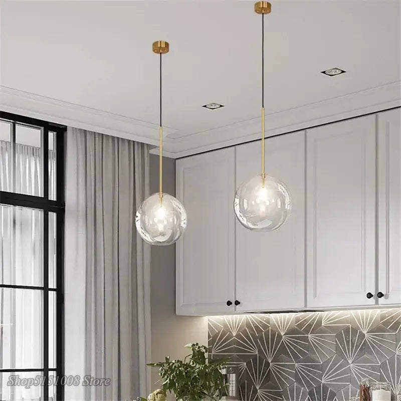 Two modern glass globe chrome pendant lights with gold fixtures and black cords hang in a dining room setting