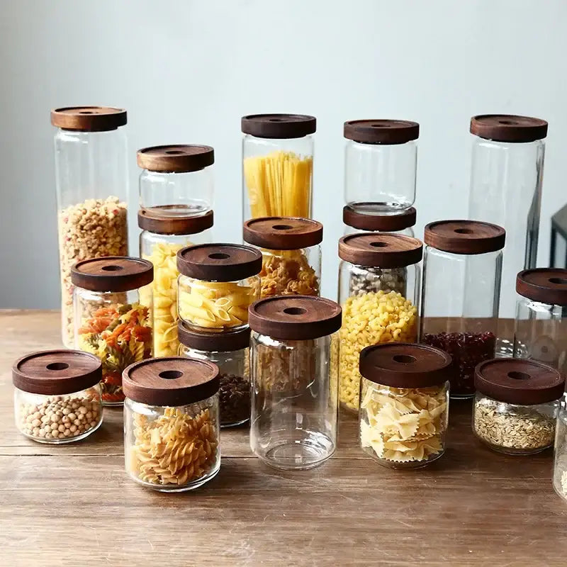 Clear glass hermetic storage jars with dark brown wooden airtight lids holding dried pasta and grains by decorbites glass hermetic