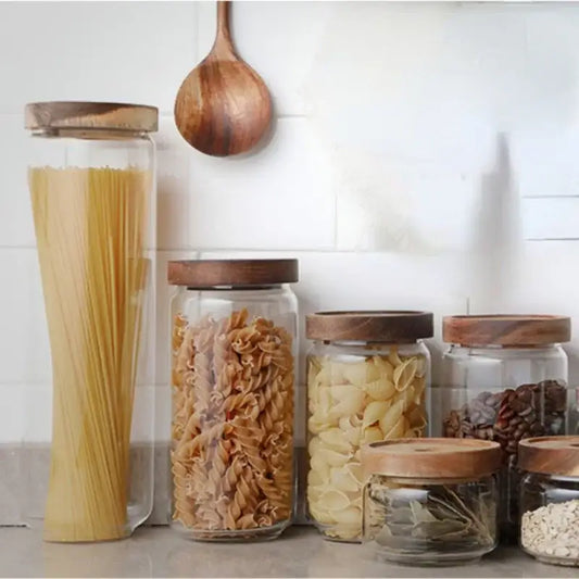Clear glass hermetic storage jars with dark wood airtight lids holding pasta and grains by decorbites
