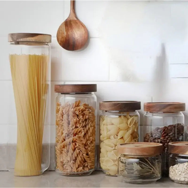 Clear glass hermetic storage jars with dark wood airtight lids holding pasta and grains by decorbites