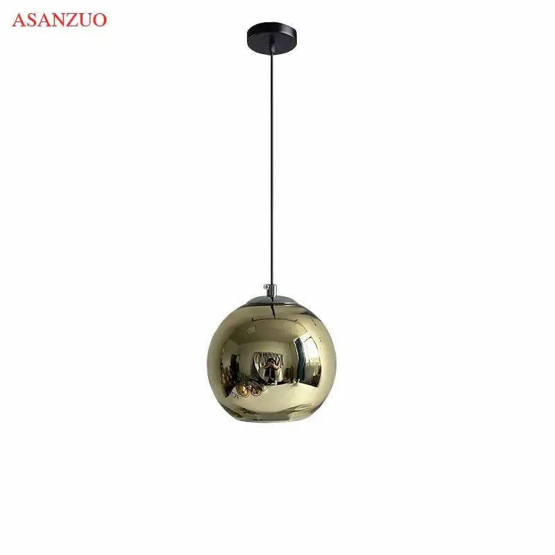 A sleek gold glass pendant light with a reflective globe and black cord for modern kitchen lighting