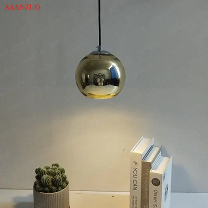 A sleek spherical gold-finished glass pendant light with reflective globe hanging from black cord for inviting atmosphere
