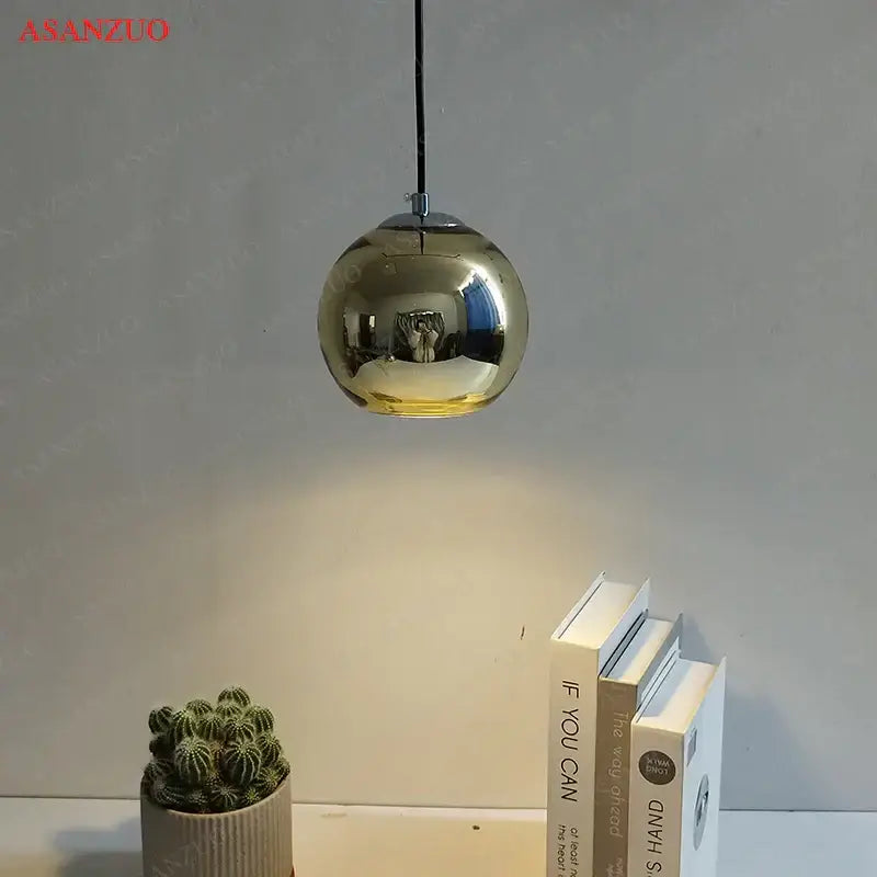 A sleek spherical gold-finished glass pendant light with reflective globe hanging from black cord for inviting atmosphere