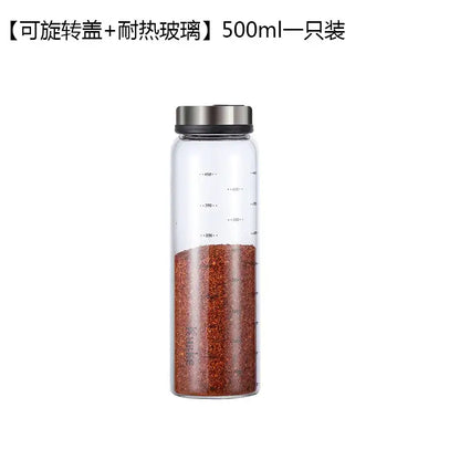A clear glass seasoning spice shaker salt with silver lid and measurement markings filled with red pepper flakes
