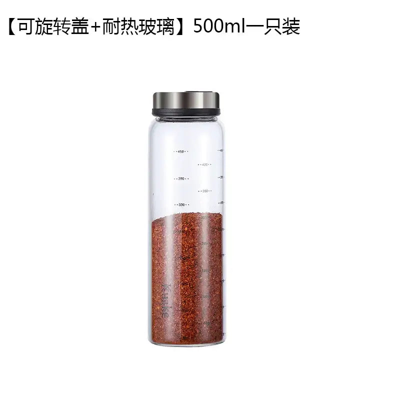 A clear glass seasoning spice shaker salt with silver lid and measurement markings filled with red pepper flakes