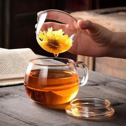 A modern clear glass tea cup with infuser and lid filled with amber glass tea for kitchen drinkware use