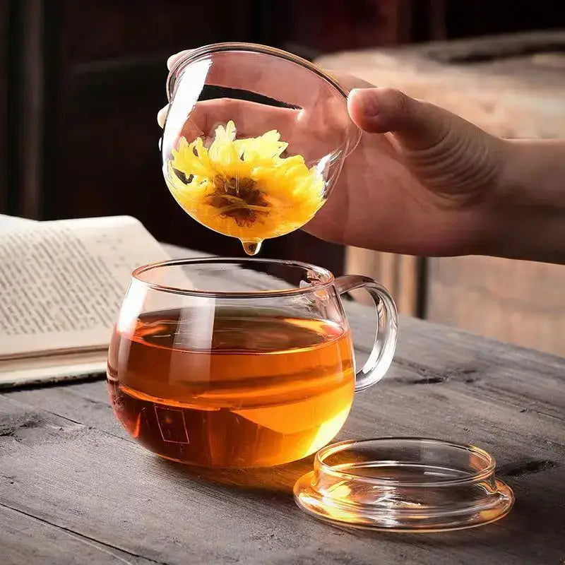 A modern clear glass tea cup with infuser and lid filled with amber glass tea for kitchen drinkware use